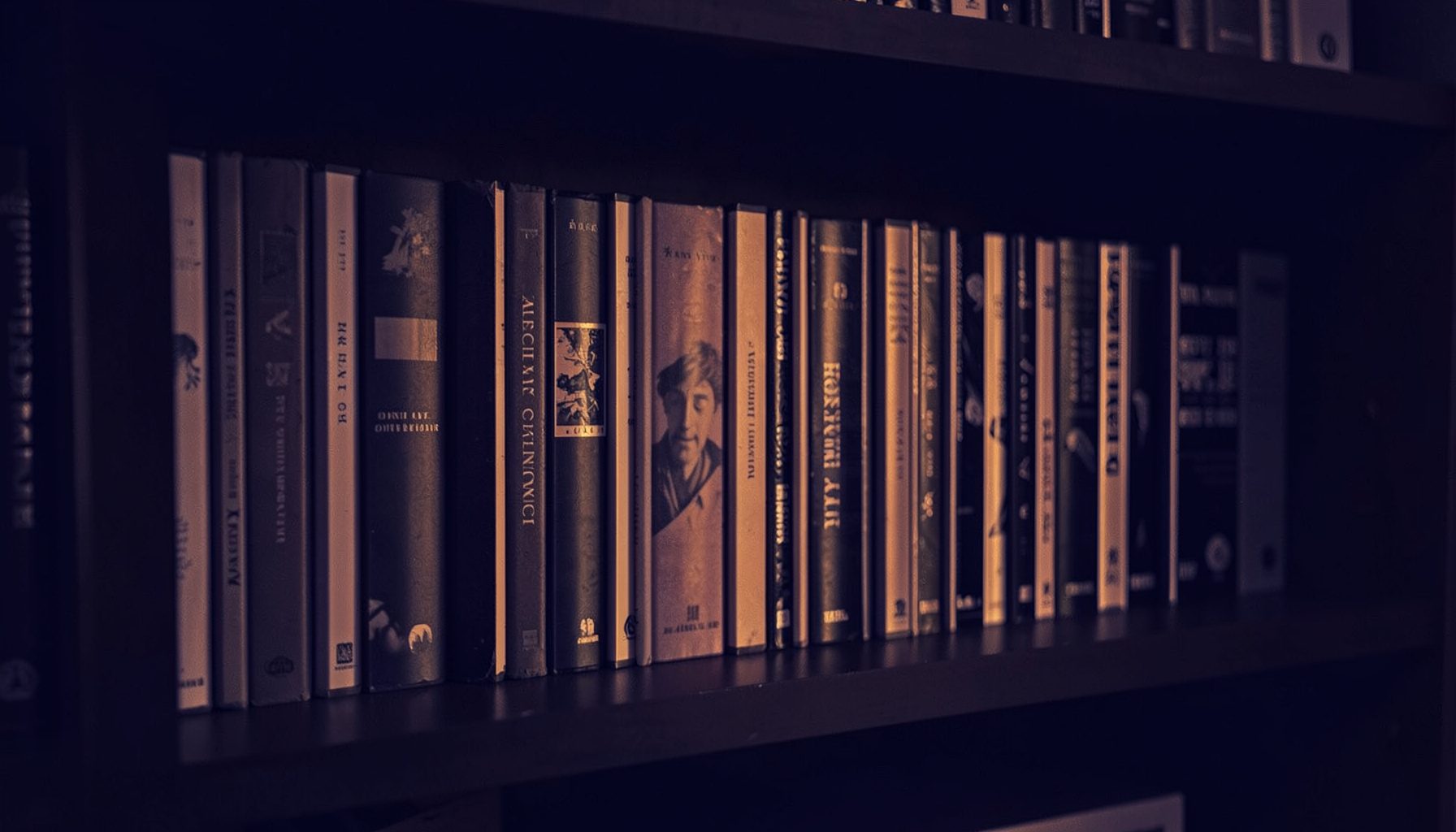A dark duotone photograph of a home media shelf lined with disc cases, deep indigo and soft amber tones, cozy evening mood.