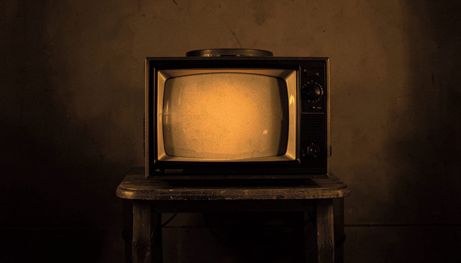 A dark duotone photograph of a vintage television set on a wooden stand, deep brown and muted gold tones, nostalgic mood.
