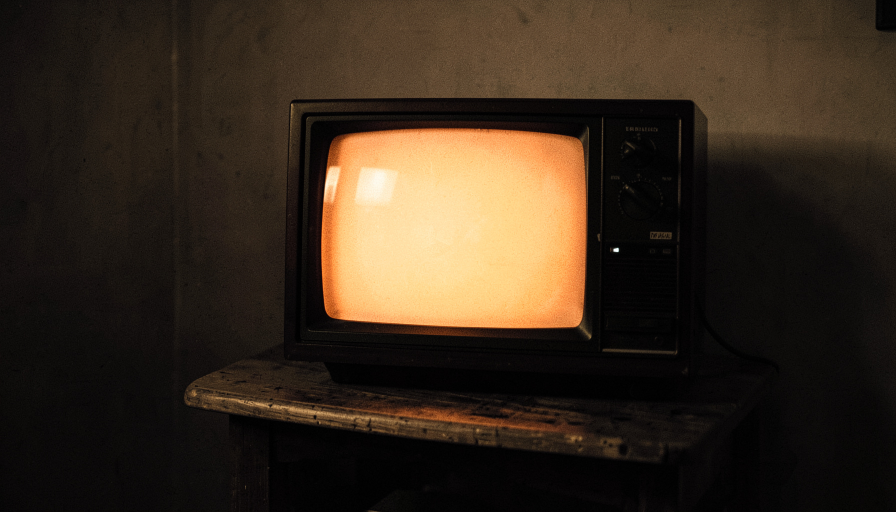 Vintage television set on a wooden stand in a dim room, screen glowing with warm light, duotone