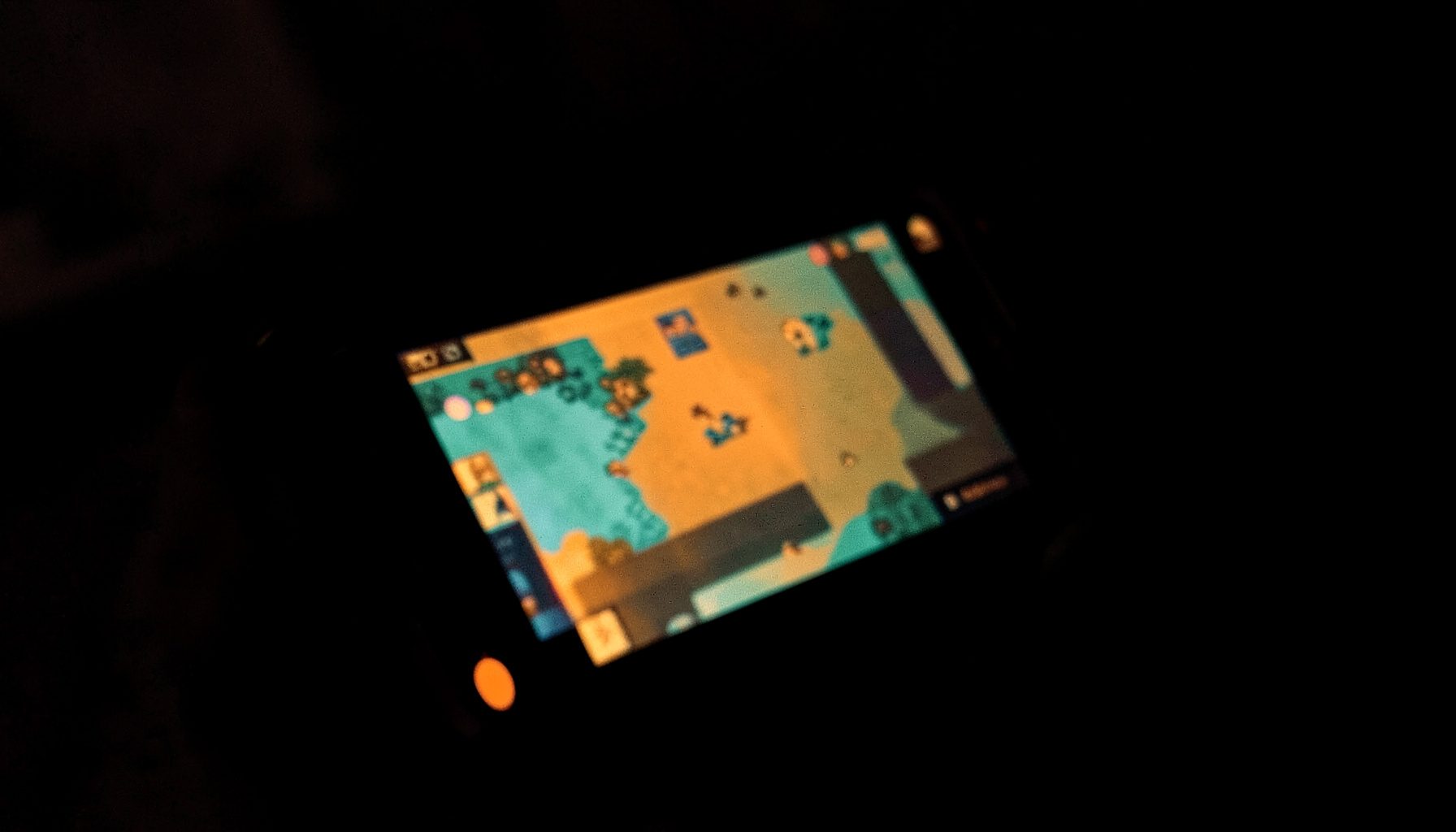 A close view of a handheld gaming device screen glowing with warm amber and teal duotone hues in a dark room.