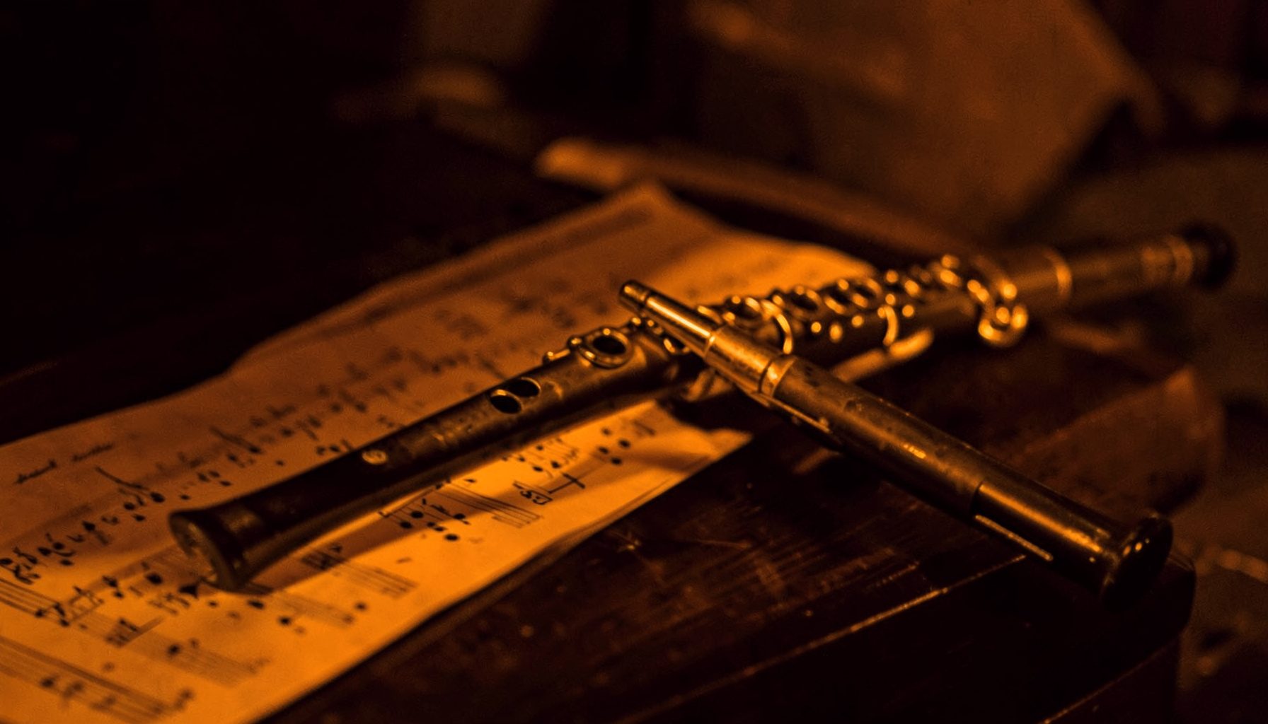 A close-up photograph of a classical flute against sheet music on a dark wooden stand, rich browns and warm gold tones in a hard two-tone duotone